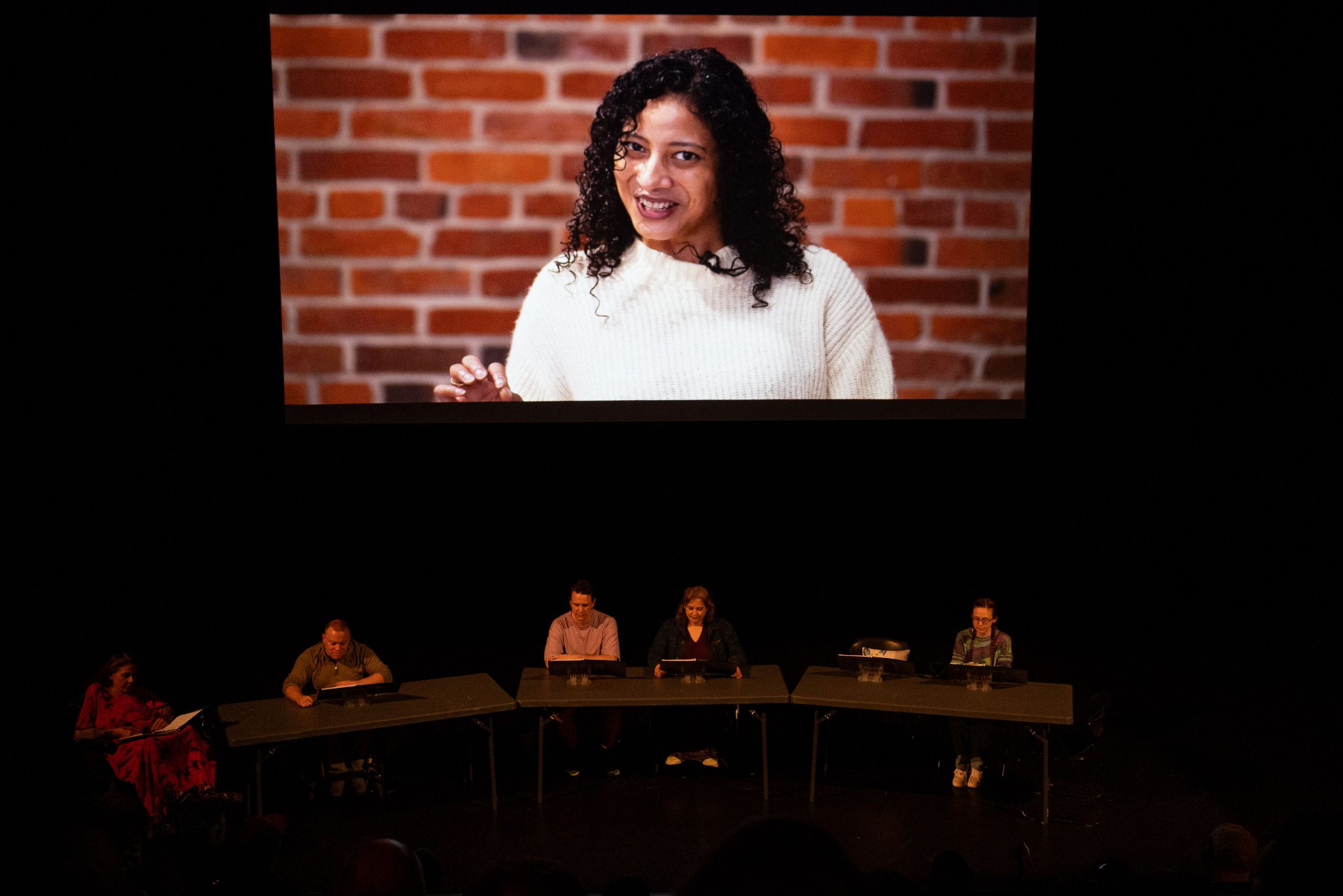 Staged Reading Photo from Saturday Nights At Axles - An actor is projected onto a screen above the rest of the cast.