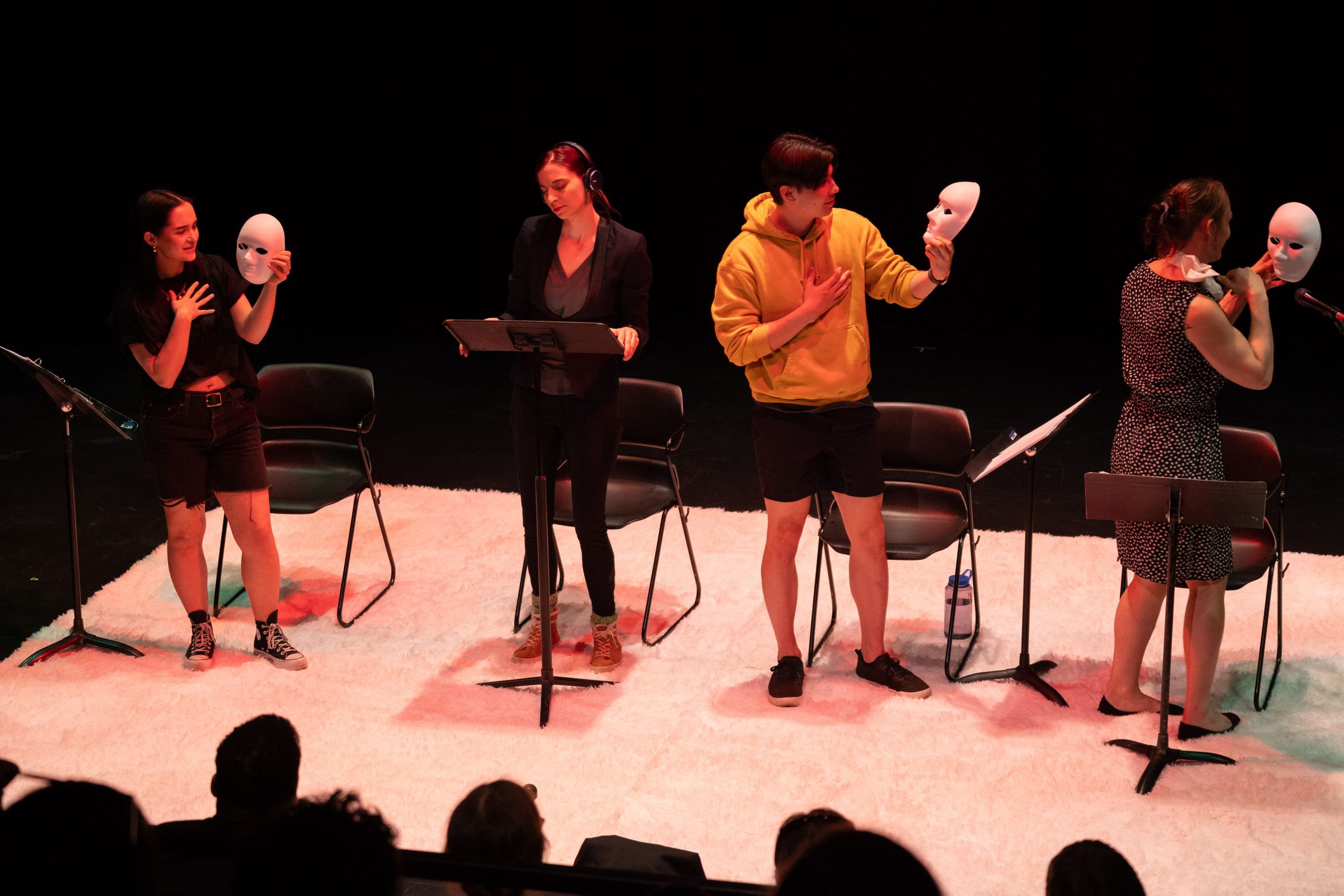 Staged Reading Photo from Faye's Room - Three actors hold up and look at white masks, the fourth is wearing headphones.