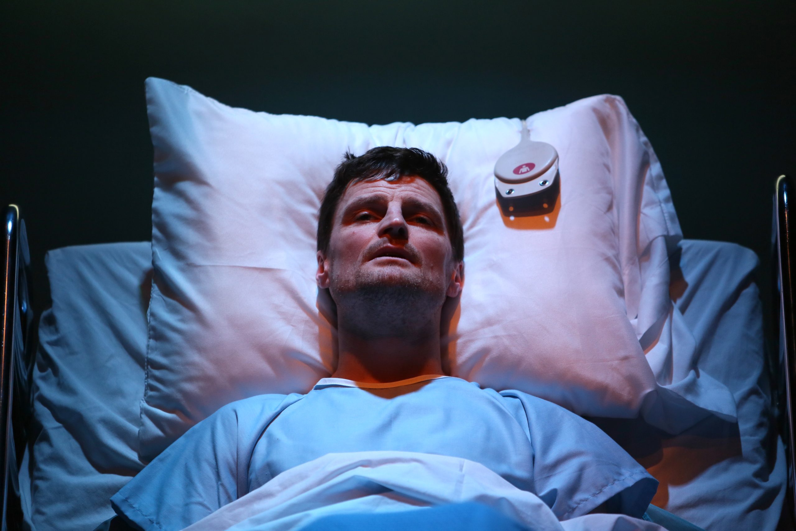 Production Photo from Whose Life is it Anyway? — An actor laying in a hospital bed.