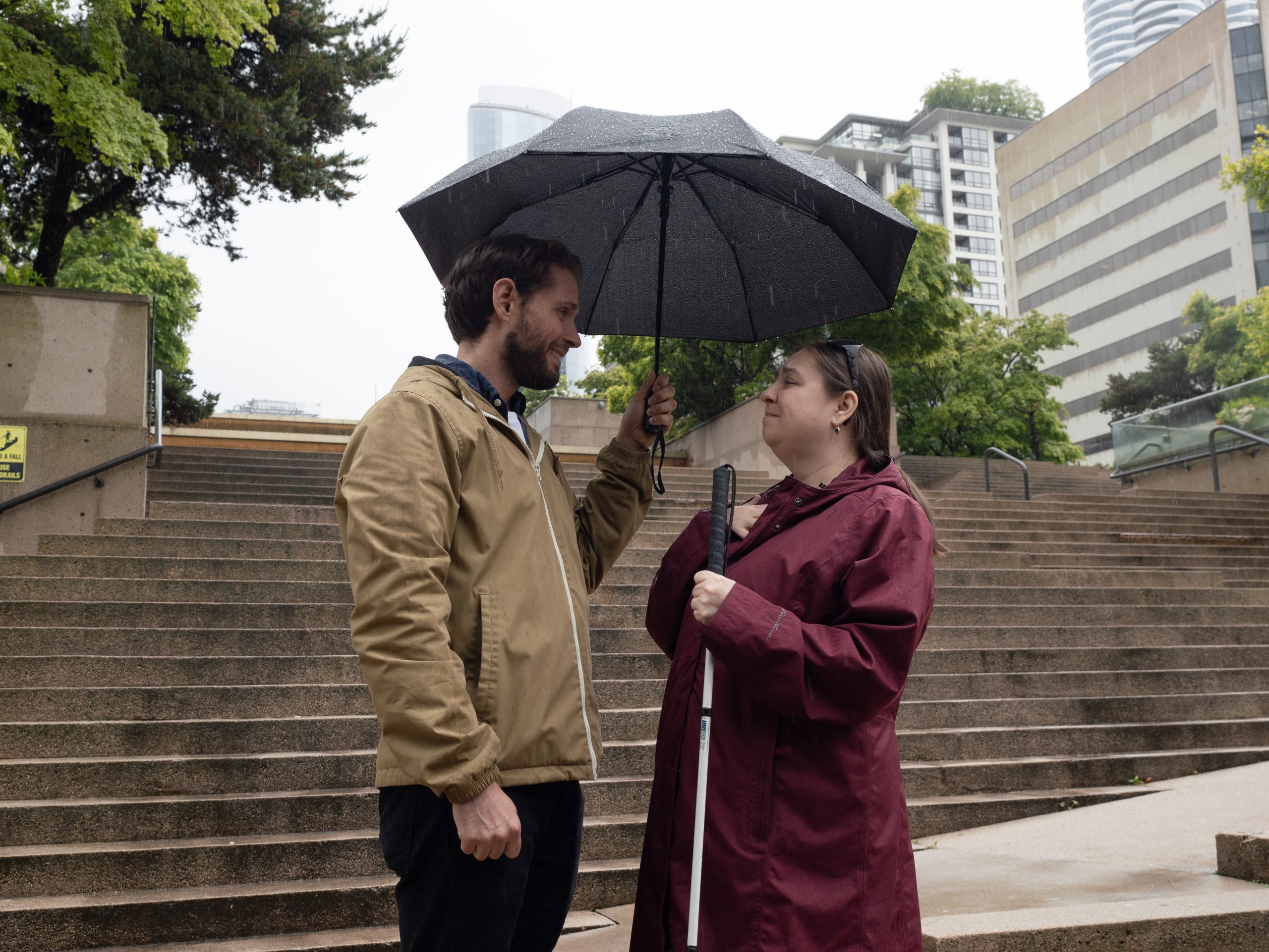 Promotional Photo for Disability Tour Bus - Two actors under an umbrella on the Robson Square “stramps”