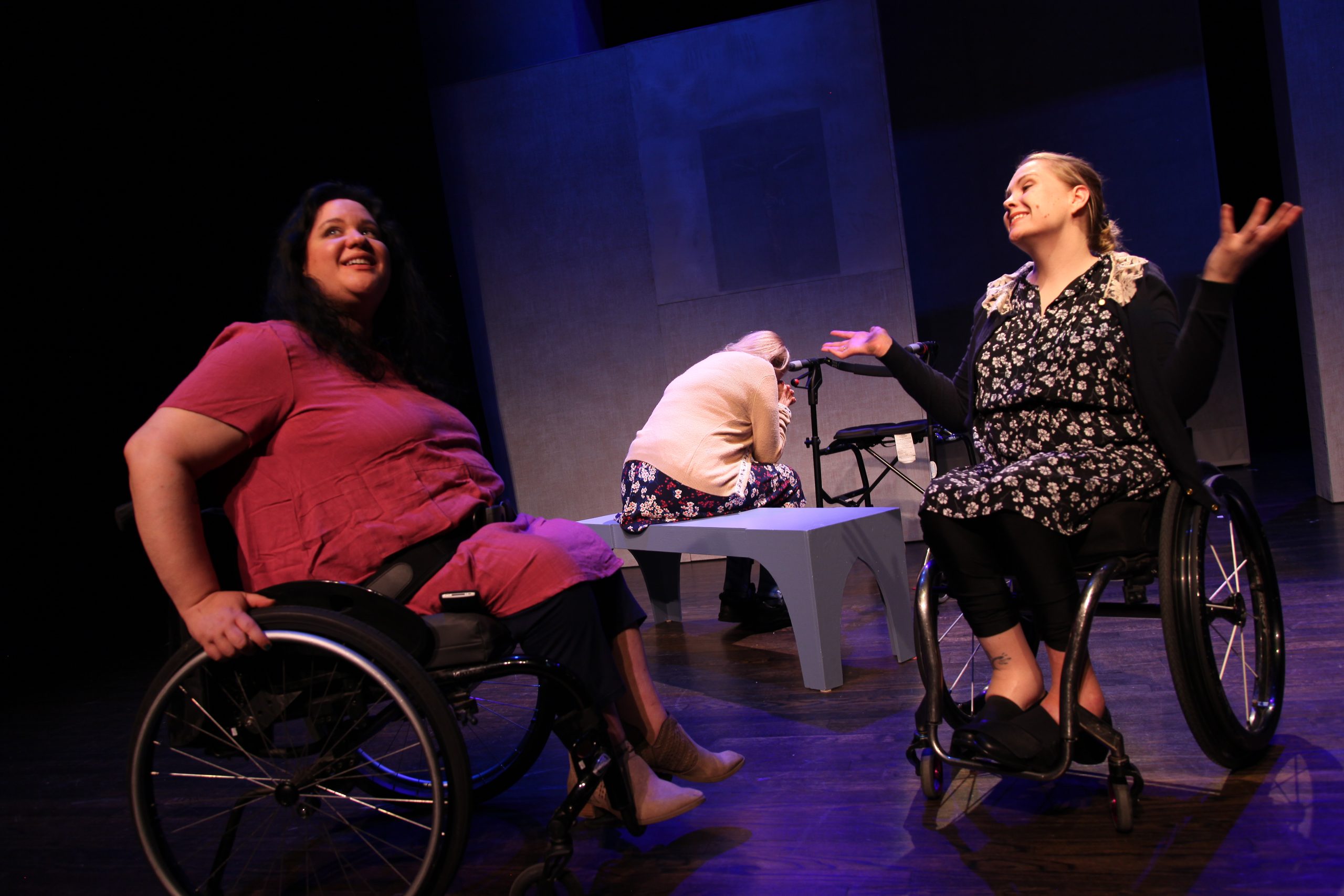 Production Photo from Act of Faith - Two actors in wheelchairs smiling and talking to each other.