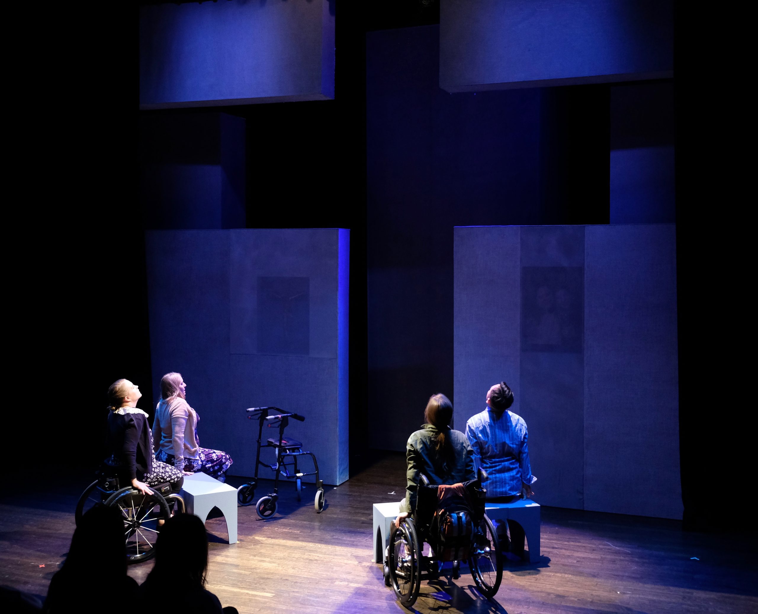 Production Photo from Act of Faith - four seated actors, two in wheelchairs, look up at a cross shape.