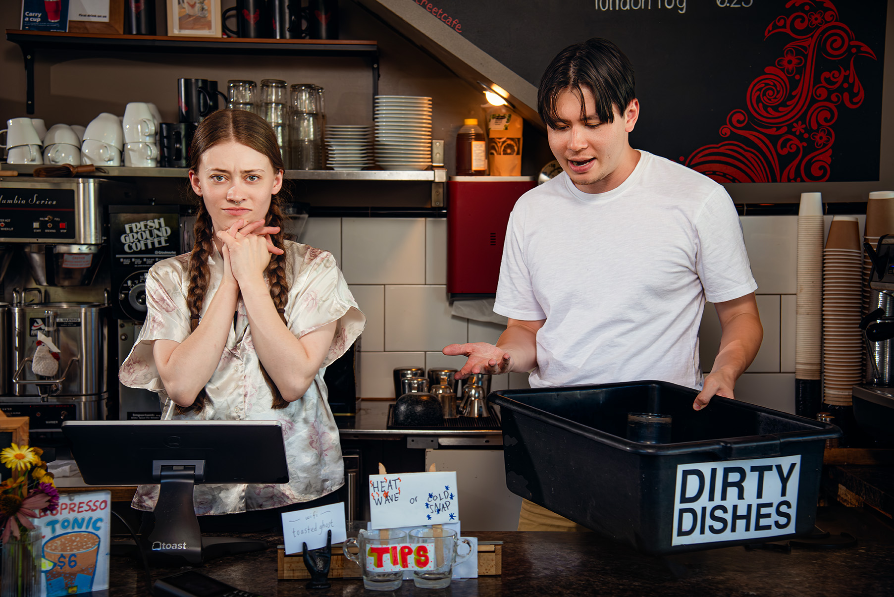 Promotional Photo of Faye's Room - Two actors in a café, one looks annoyed, the other is clueless