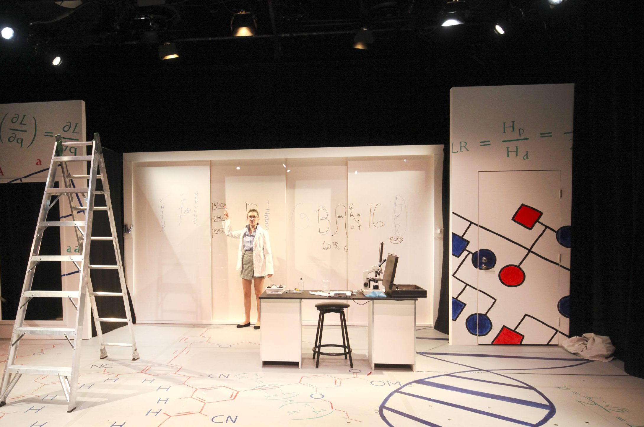 Production Photo from Sequence - An actor in science lab set, in front of a whiteboard.