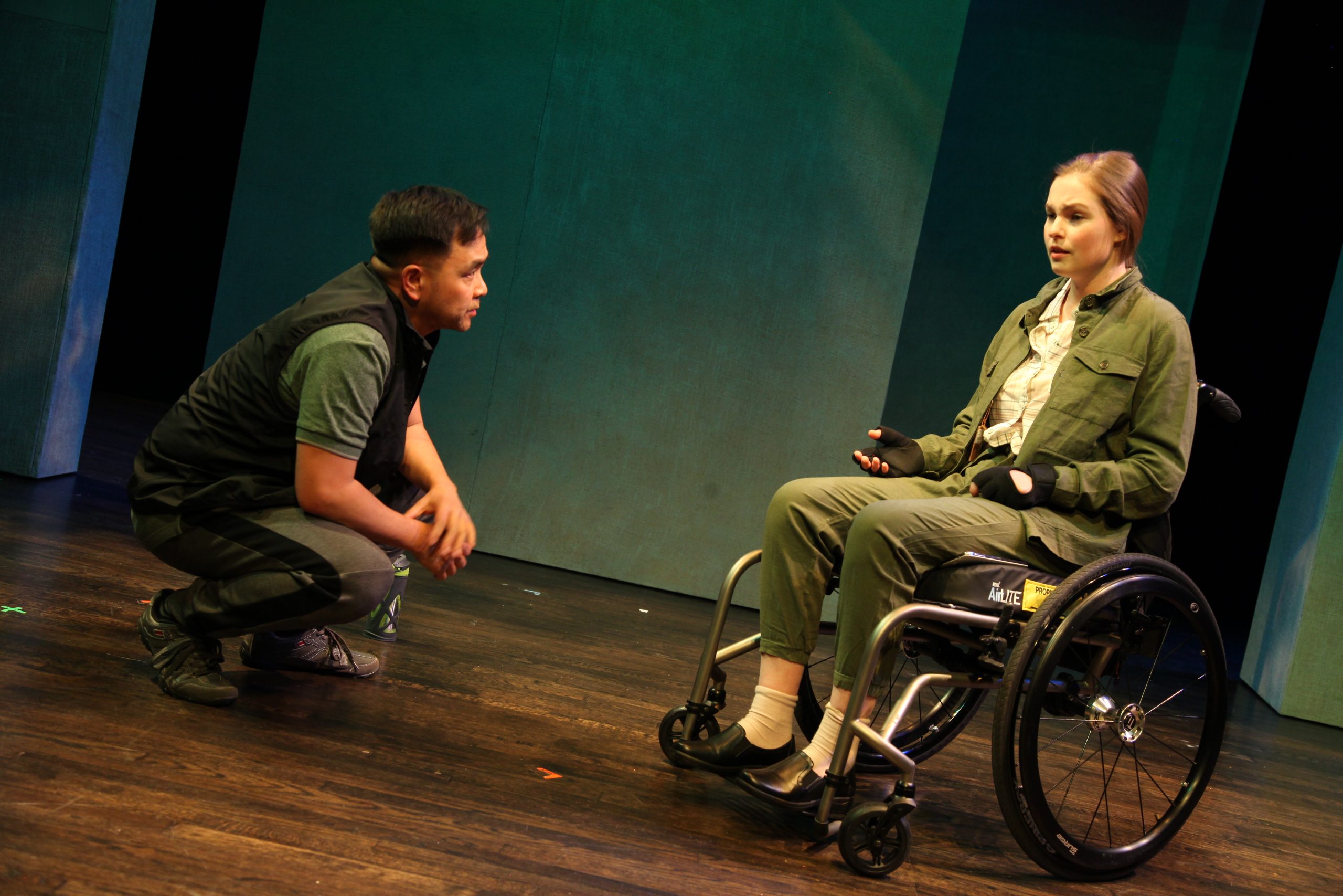 Production Photo from Act of Faith - Two actors - one in a wheelchair, one bending down, listening to other carefully.