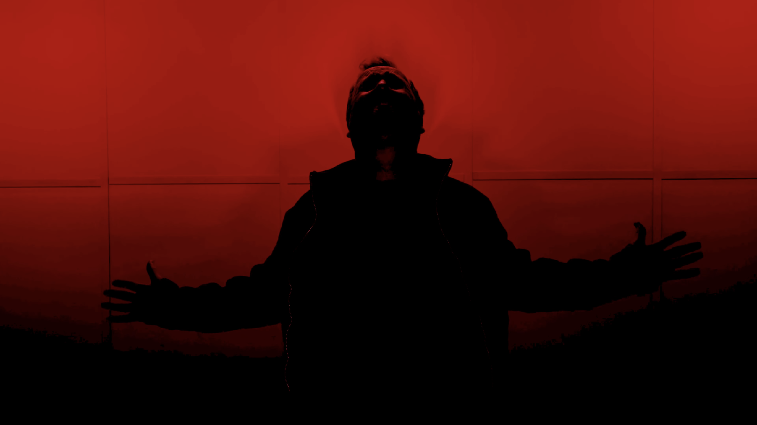 Screengrab from In Camera - an actor backlit with red lighting, his arms outstretched.